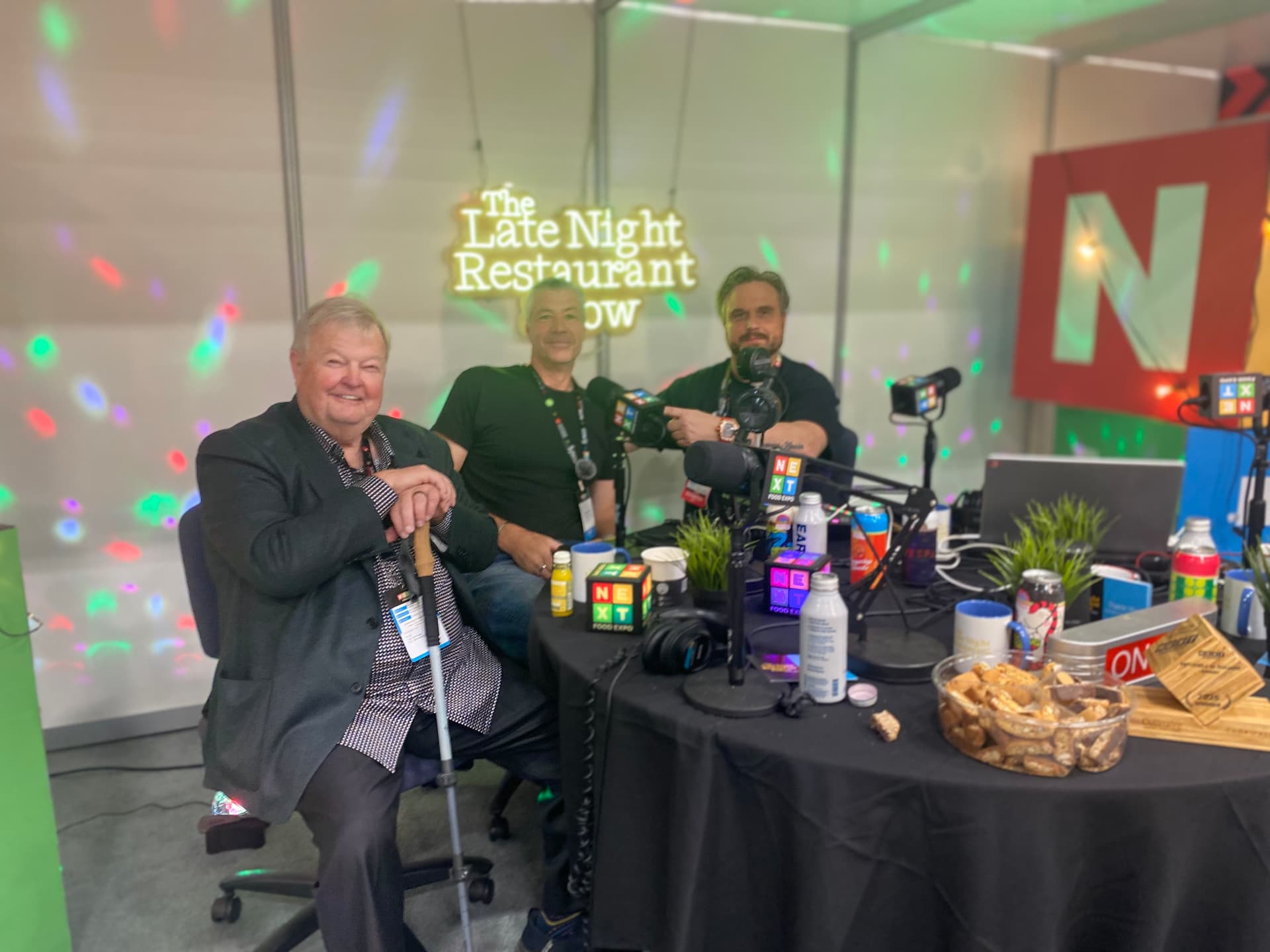 Three guests around The Late Night Restaurant Podcast table with the neon sign glowing behind them