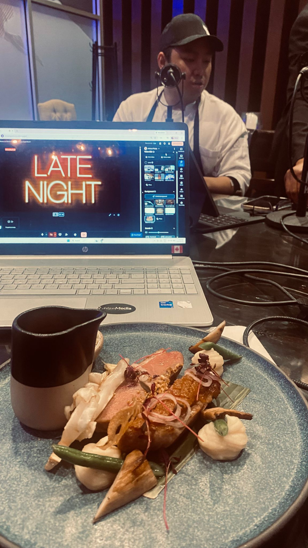 A plated chef's dish in front of a laptop showing The Late Night Restaurant Podcast neon logo